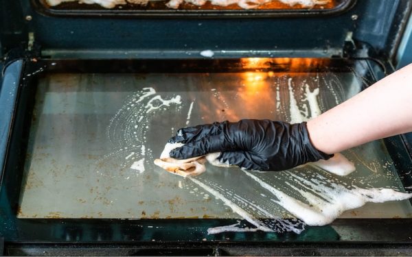 Cách vệ sinh lò nướng Bosch đúng chuẩn & lâu bền 4 Tay đeo găng tay đang thoa hỗn hợp baking soda lên thành lò nướng Bosch